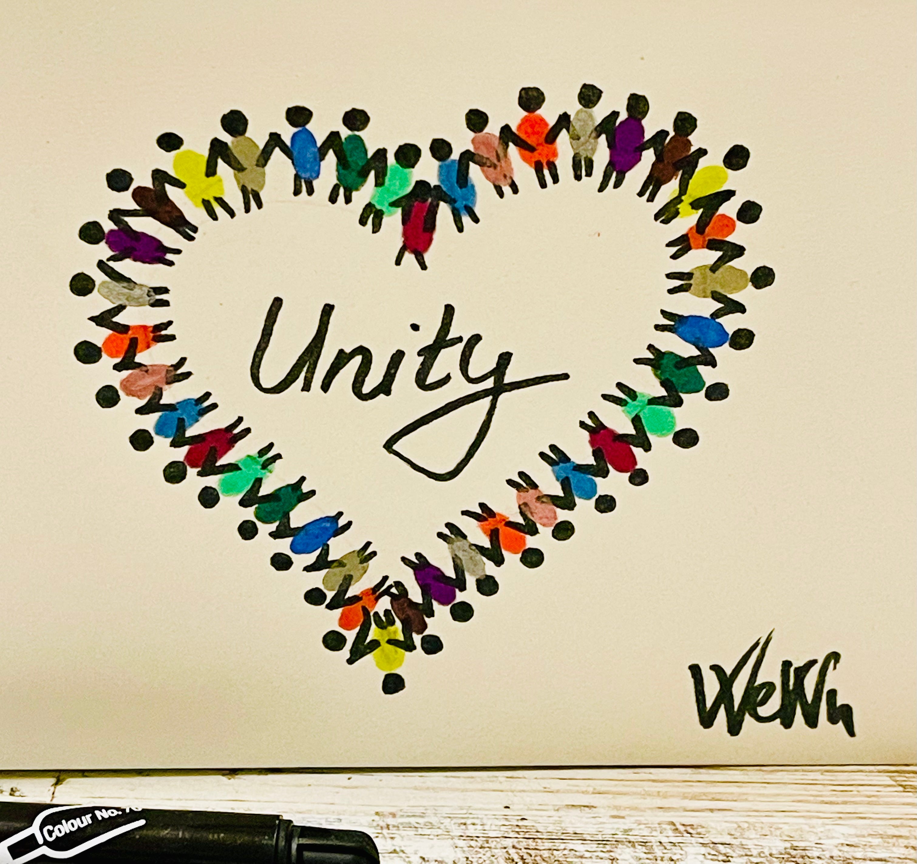 Heart shape made of colorful paper cutouts with 'Unity' text and a pen on a wooden surface.